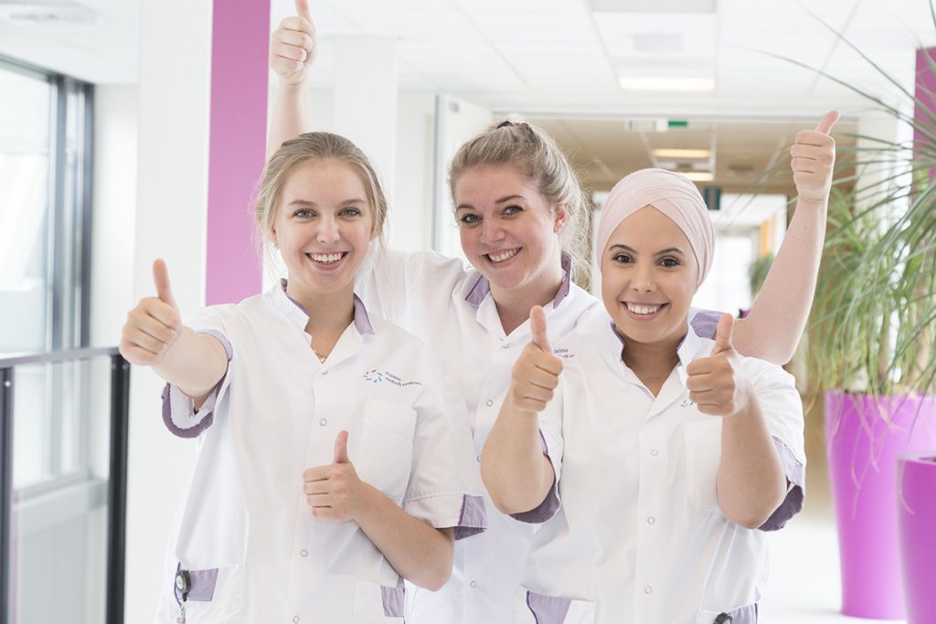 drie blije verpleegkundigen steken hun duimen op